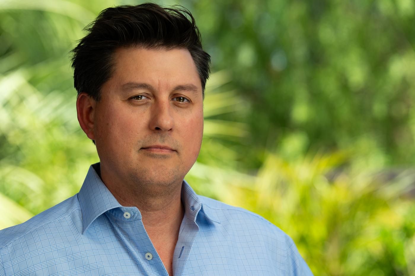 Joaquin, an executive who lives with MS, poses in a blue button-up shirt in his backyard.