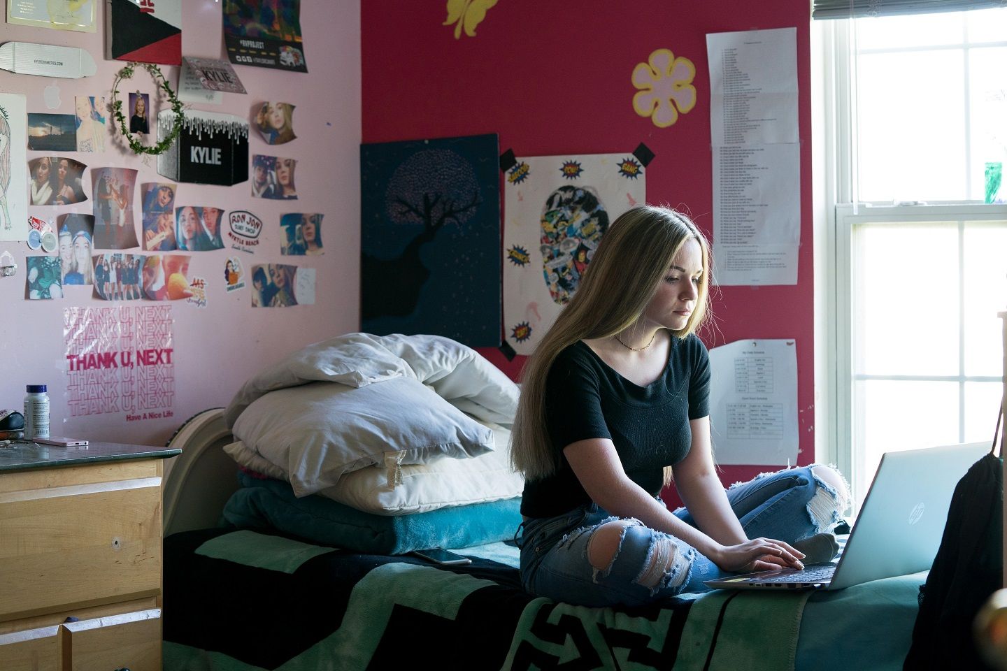 A teenage girl who lives with MS sits on her bed typing on her laptop.