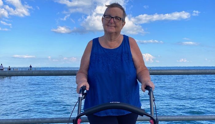 Faith, a woman who lives with MS, stands with her walker in front of a lake.