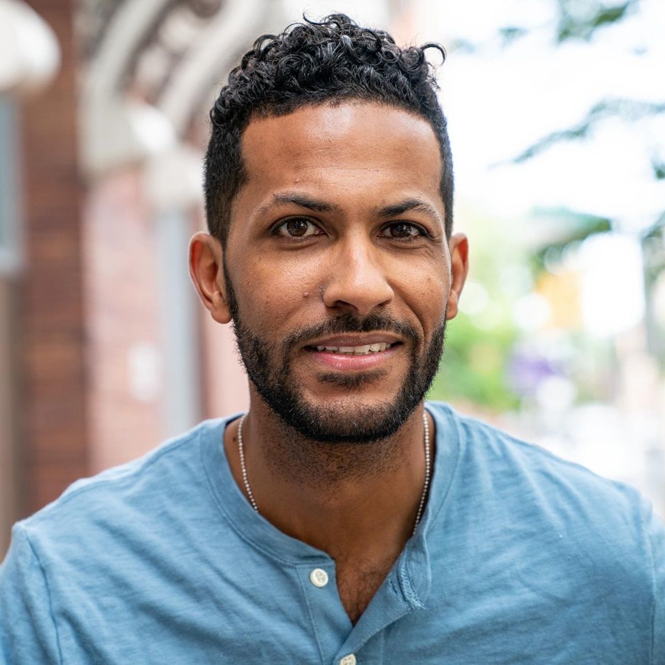 Kenneth, a man with MS, smiling in a blue shirt in front of a brick wall.