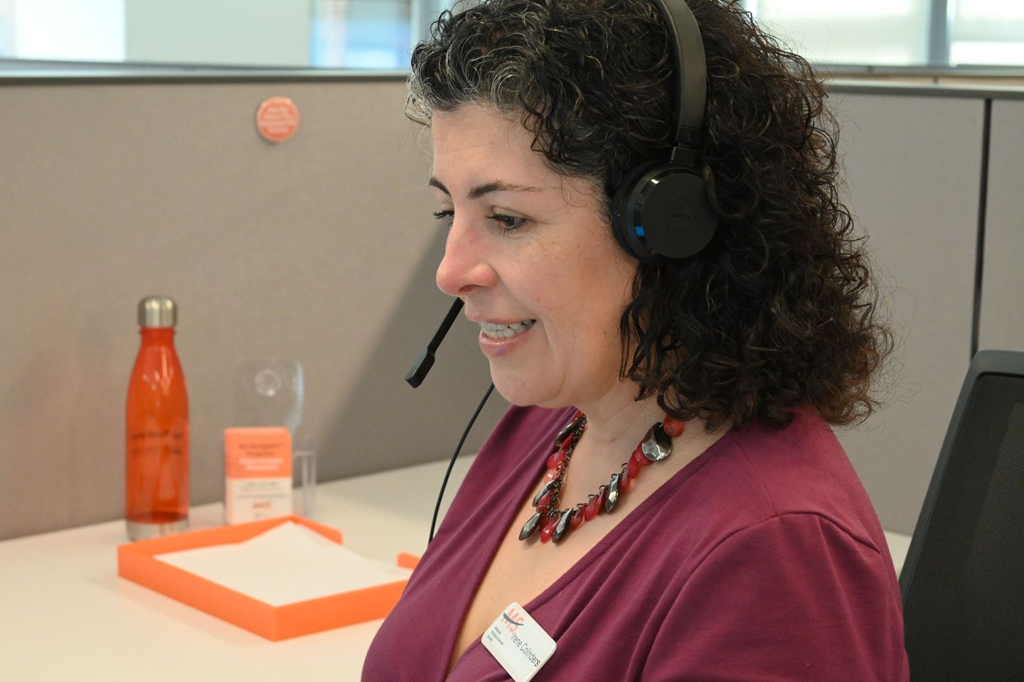 Una mujer con audífonos sonríe mientras mira hacia abajo en una oficina.