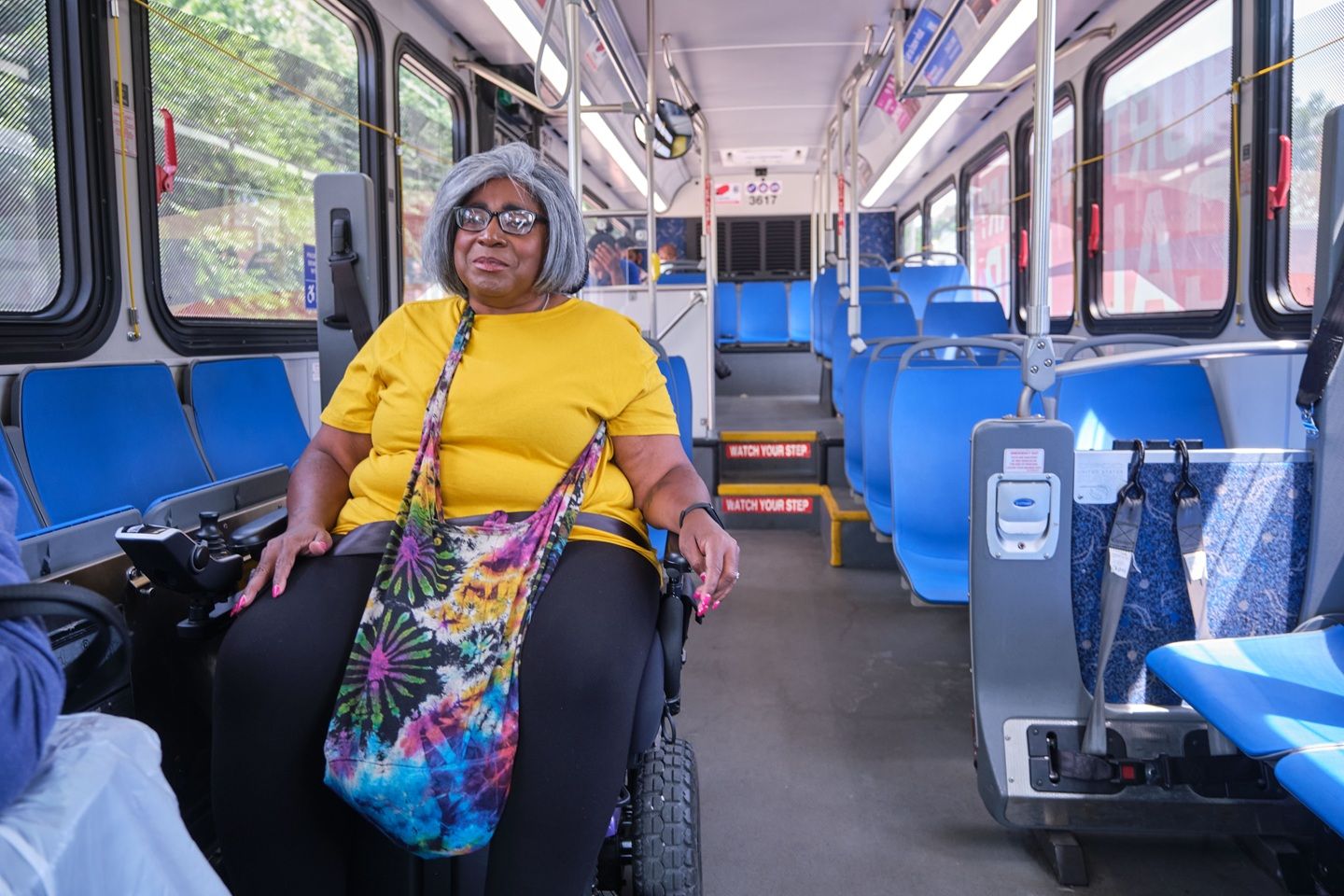 A woman with MS using a wheelchair while siting in an accessible area of a public bus.