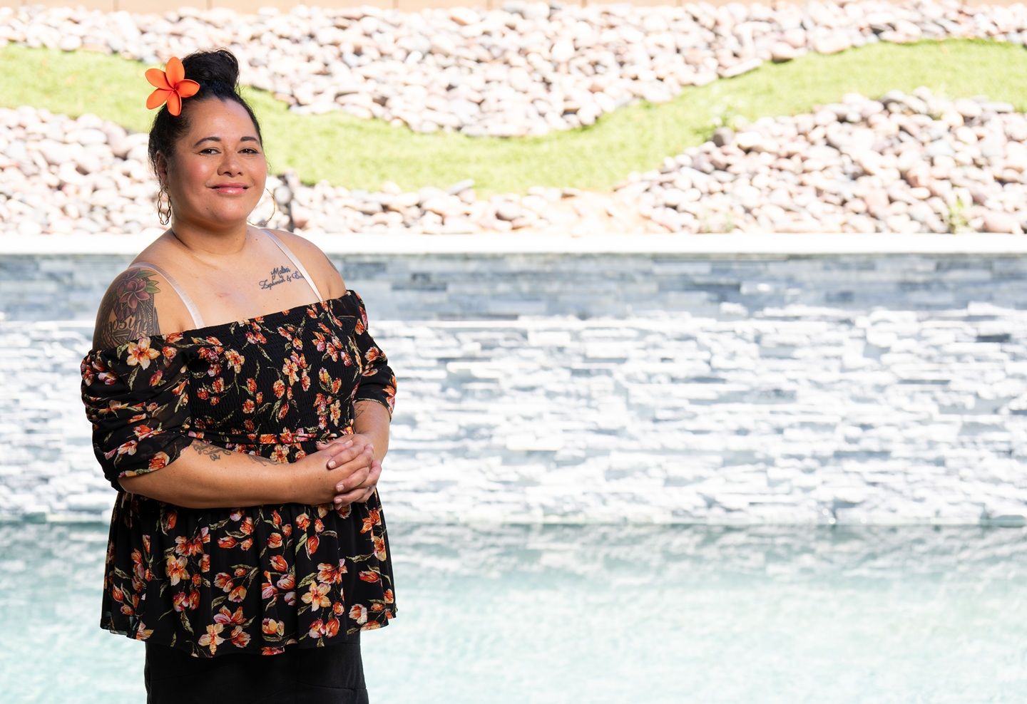 Una mujer con moño y una flor en la cabeza sonríe frente a una playa.