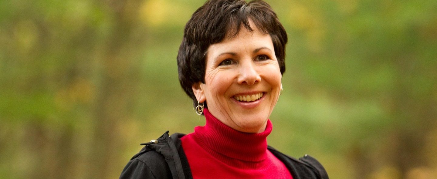 A woman with short brown hair who lives with MS smiles outdoors.