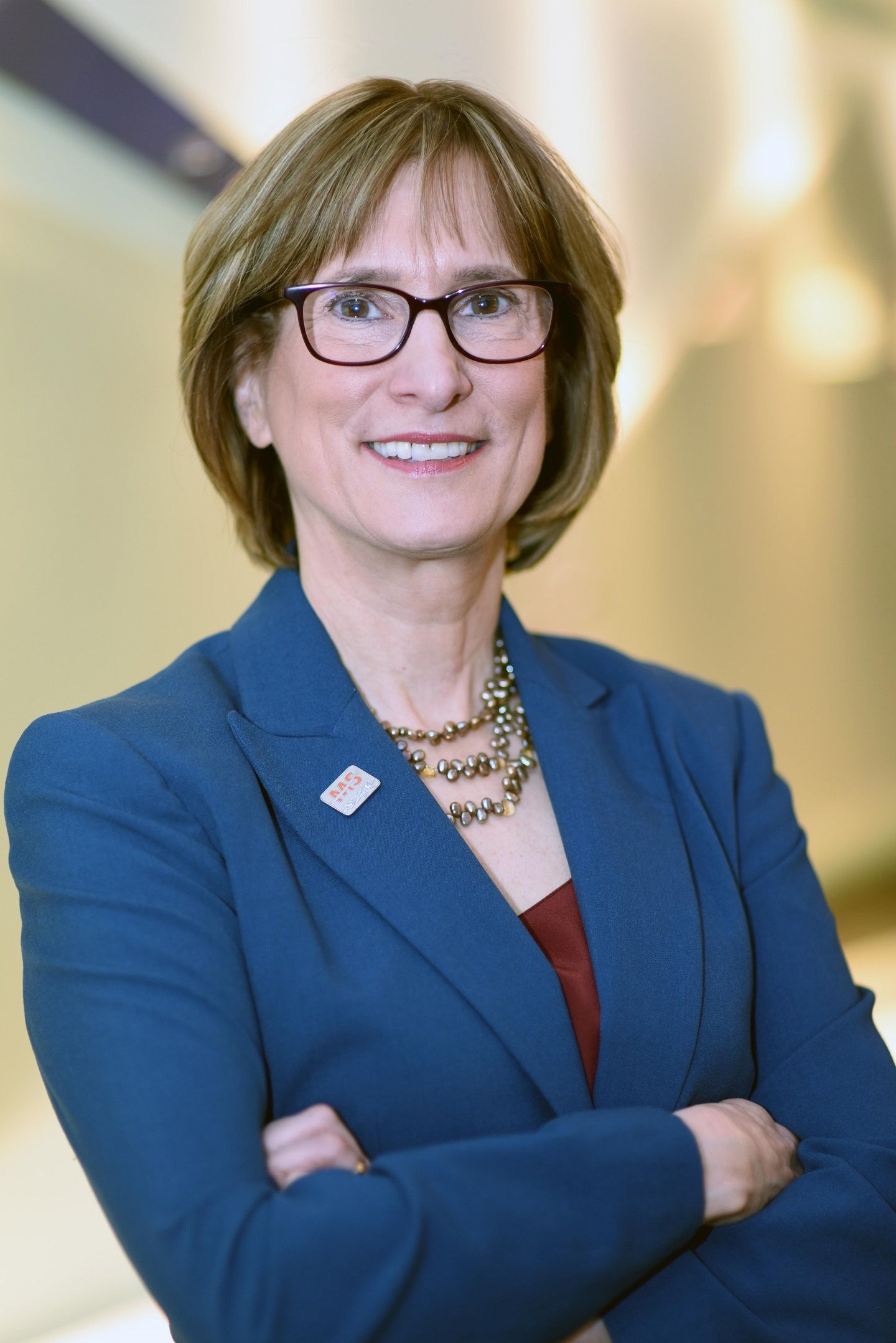 A woman with bobbed hair in a blue blazer, the CEO of the National MS Society, stands smiling with her arms crossed.