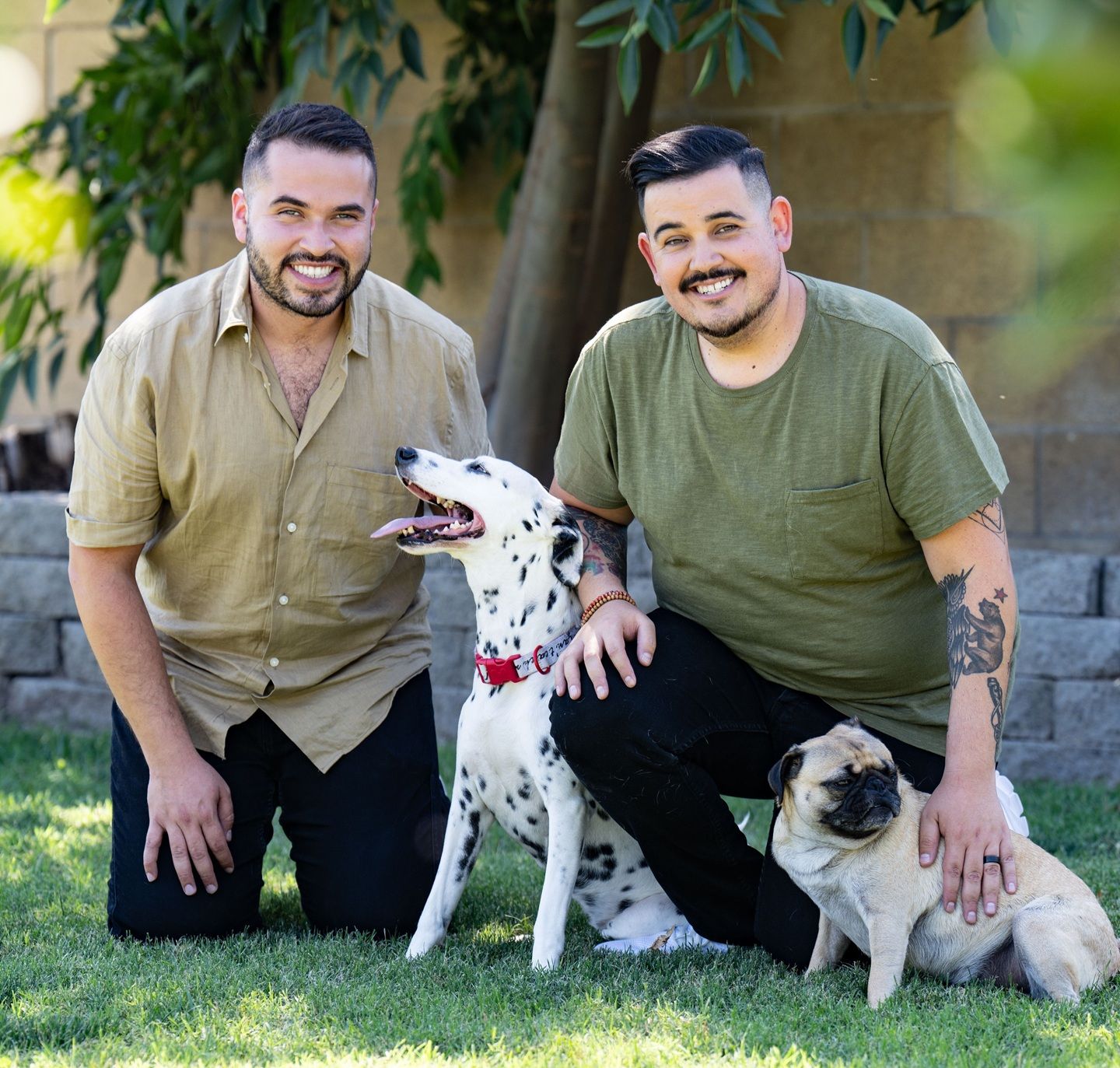 Two men, one with multiple sclerosis, smile and kneel with two dogs in a garden.