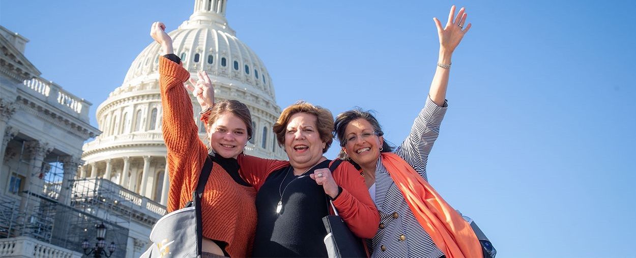 Three generations of MS advocates affected by MS raise their arms in triumph before the U.S. capitol dome.