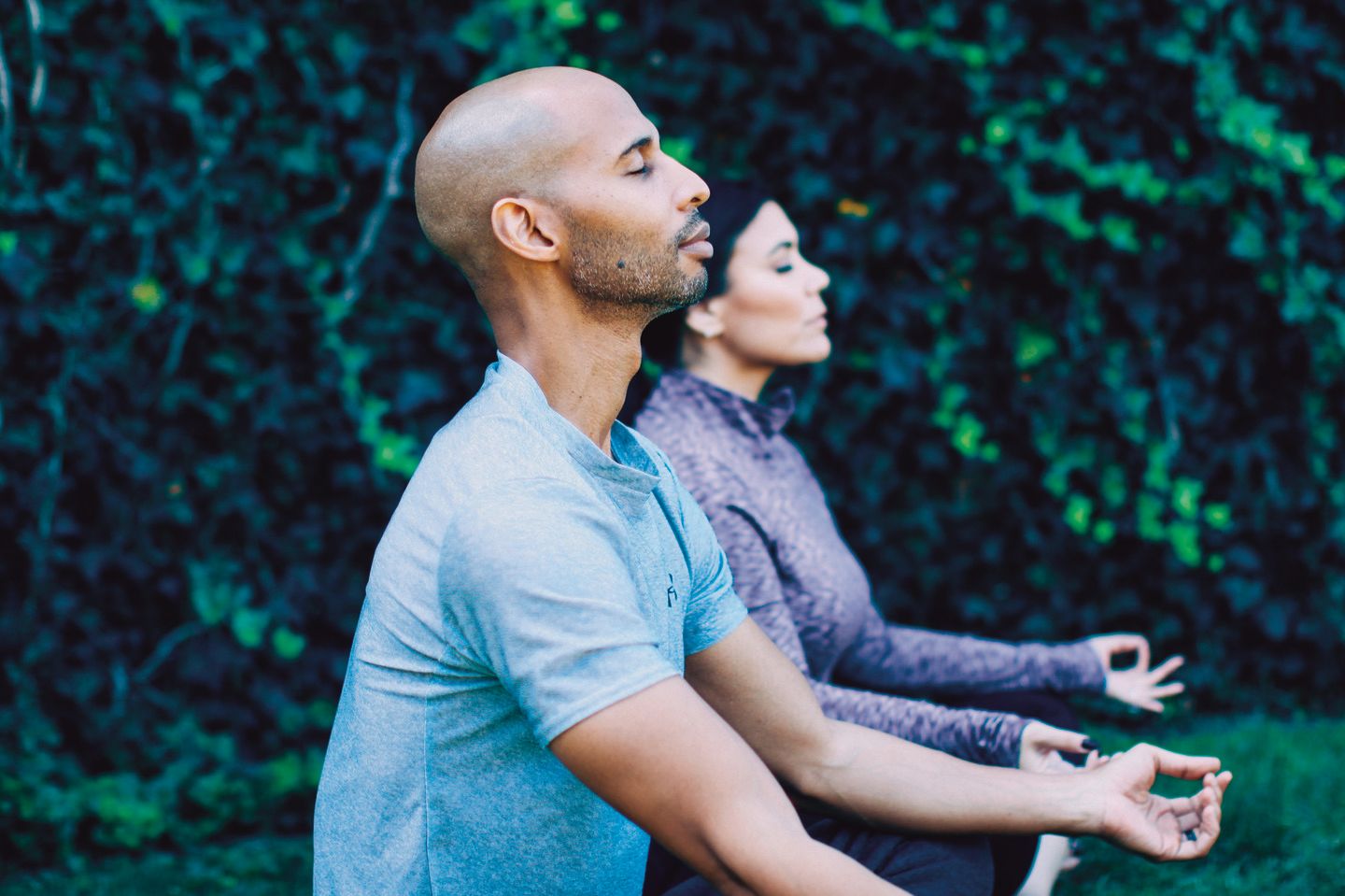 Two people sit outside in a meditative pose with eyes closed and peaceful facial expressions.