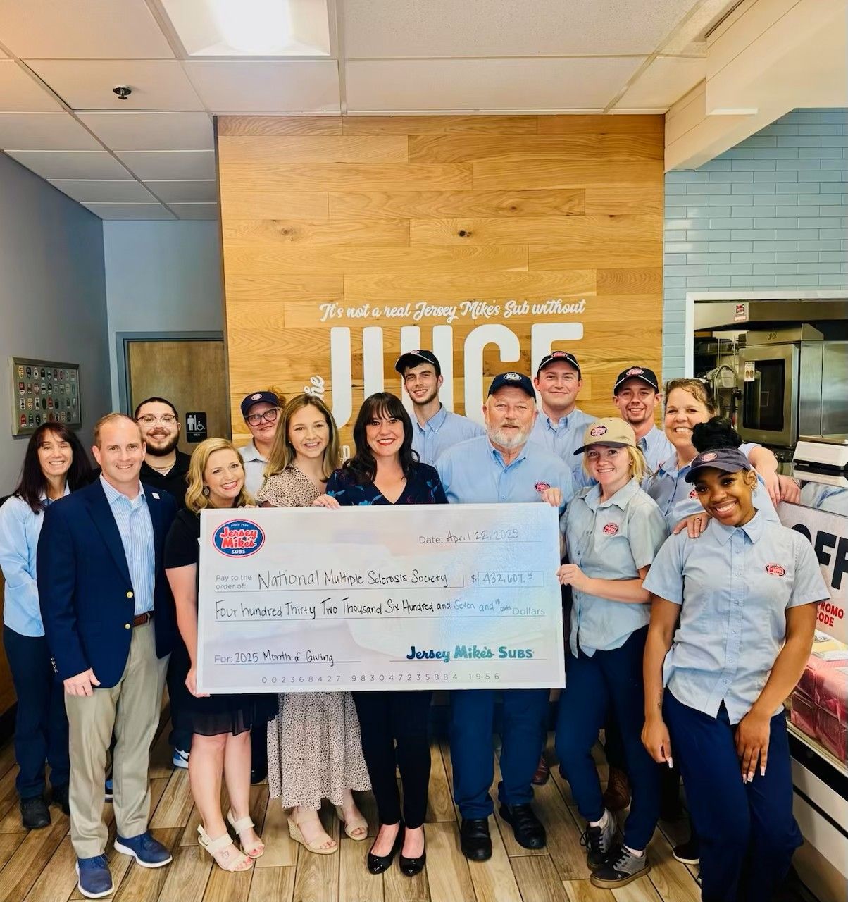 A group of Jersey Mike's Subs and National MS Society representatives hold an oversized check in a Jersey Mike's restaurant
