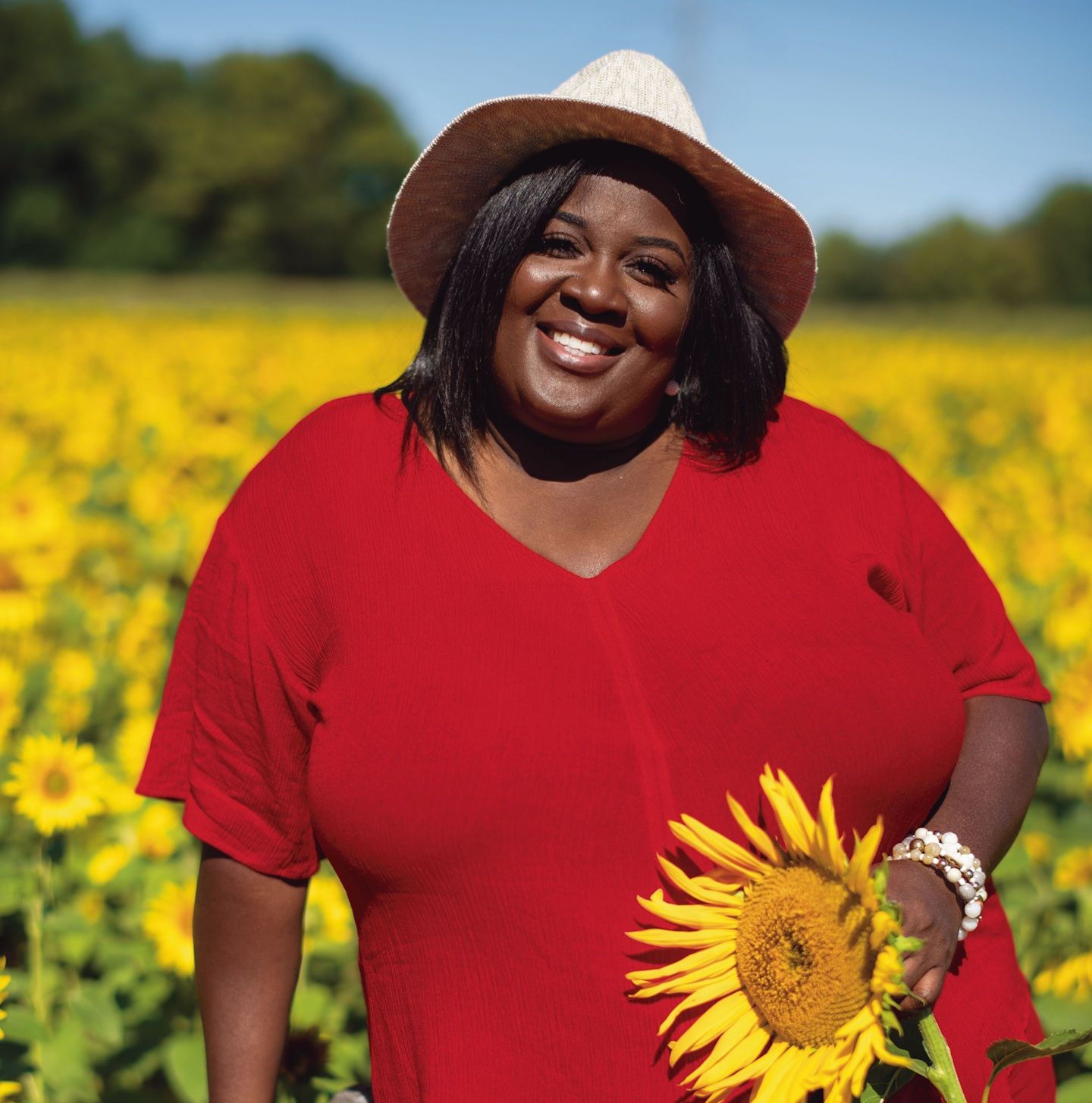 Nicole White standing in a field holding a sunflower.