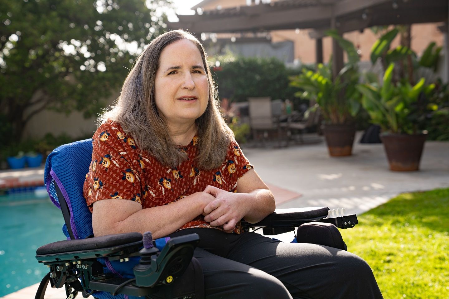 Una mujer de cabello largo está sentada en una silla de ruedas frente a una alberca.